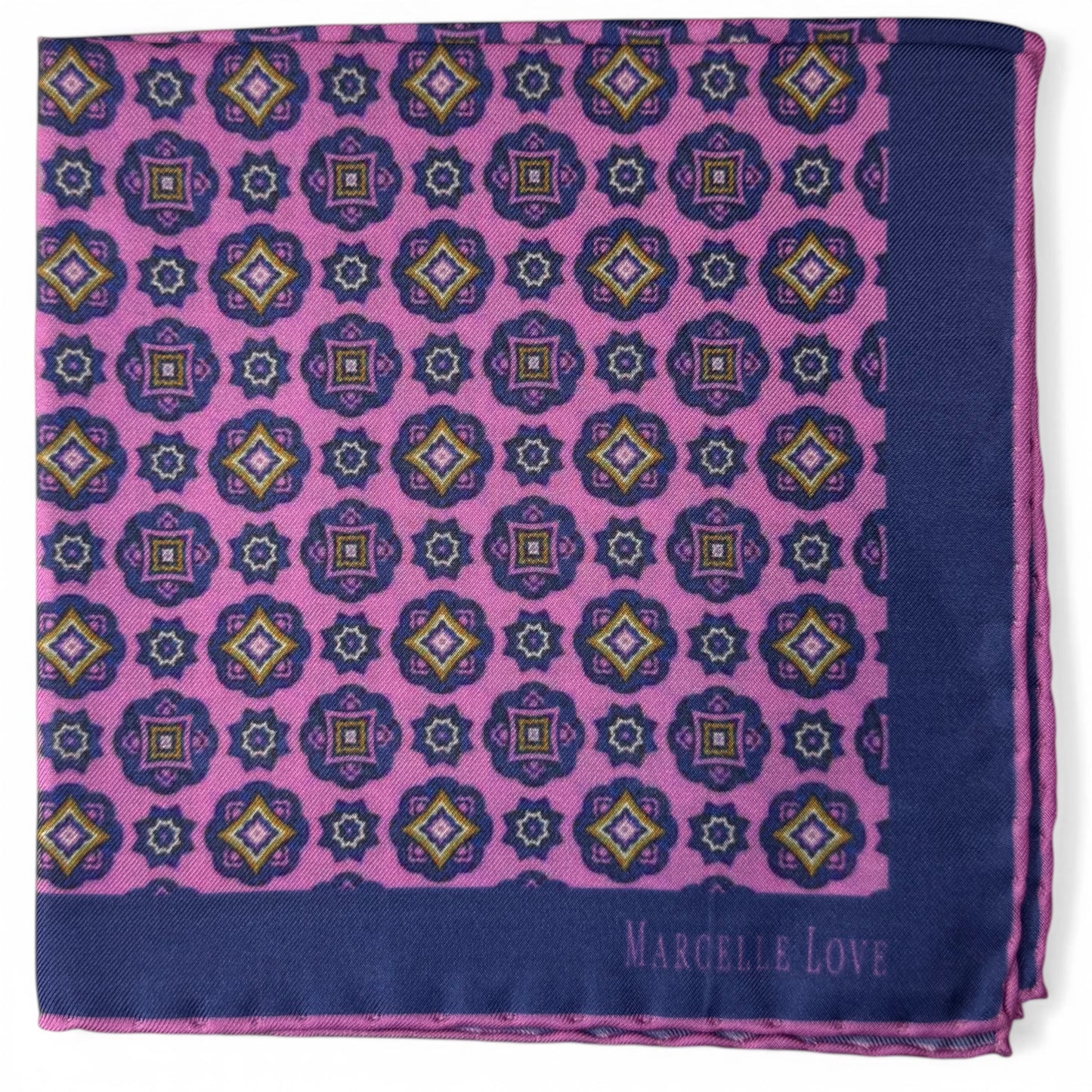 Patterned fabric square with geometric design on a pink and blue background, featuring the brand 'Marcelle Love'.