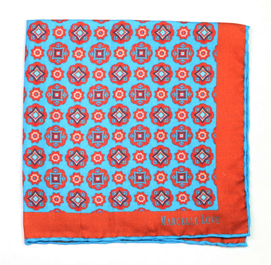 A pocket square with a floral and diamond pattern, predominantly red and blue, with the brand name 'MARCELLE LOVE' printed at the lower right corner.