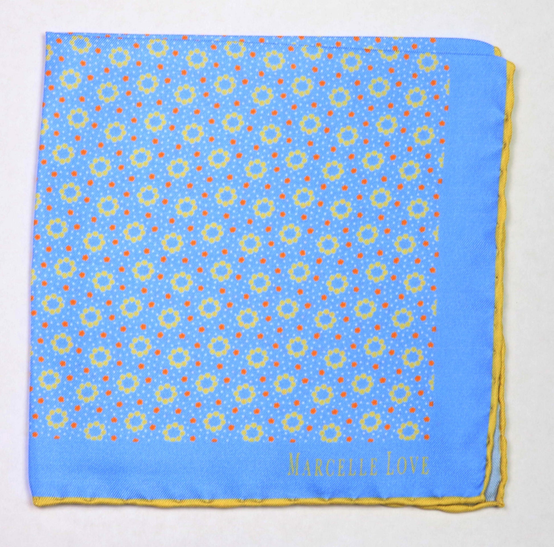 A blue pocket square with a white floral and dot pattern, and 'MARCELLE LOVE' printed at the lower right corner.